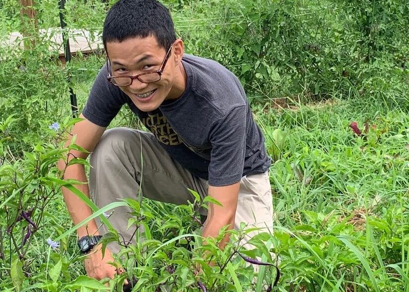 Smiling teenager kneeling as he works in a garden