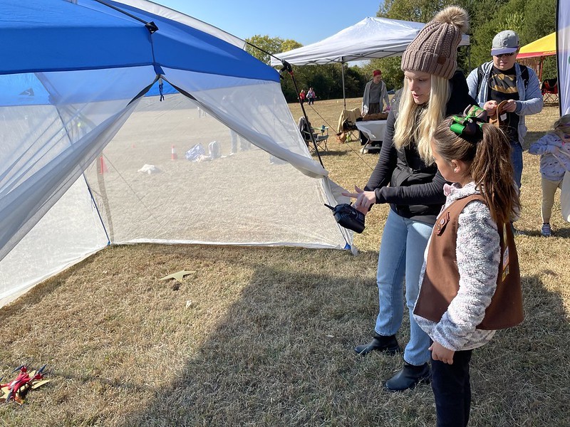 A woman shows a young Girl Scout how to fly a drone in an screen house tent.