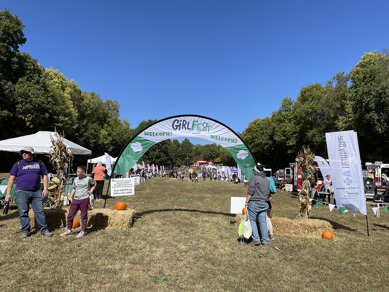 An arched banner creates an entrance to two rows of pop up tents housing hands-on learning activities in an outdoor setting on a sunny day.