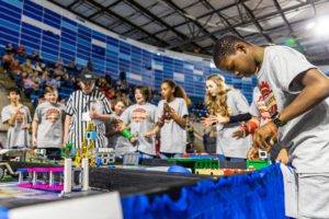 Team of seven boys and girls around a FIRST LEGO League game table with a referee