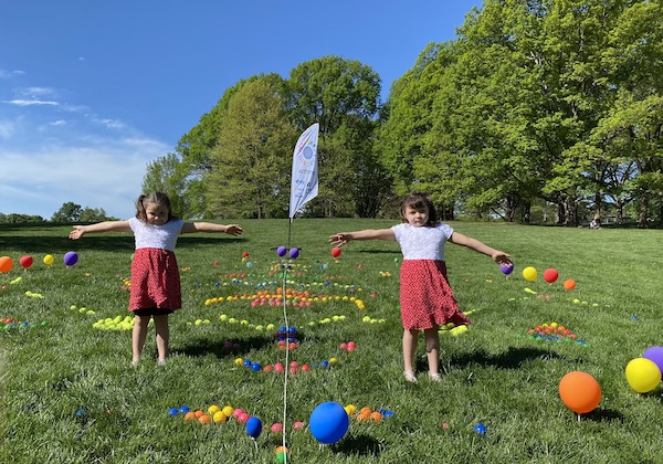 Two young girls stretch out arms in grassy field with multi-colored balls to demonstrate symmetry.