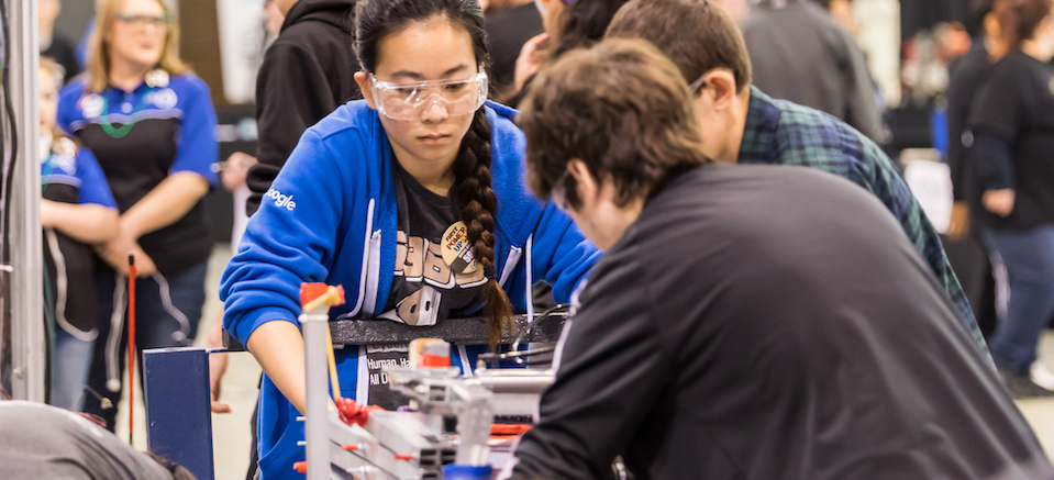 A female and male high school student transport a robot.