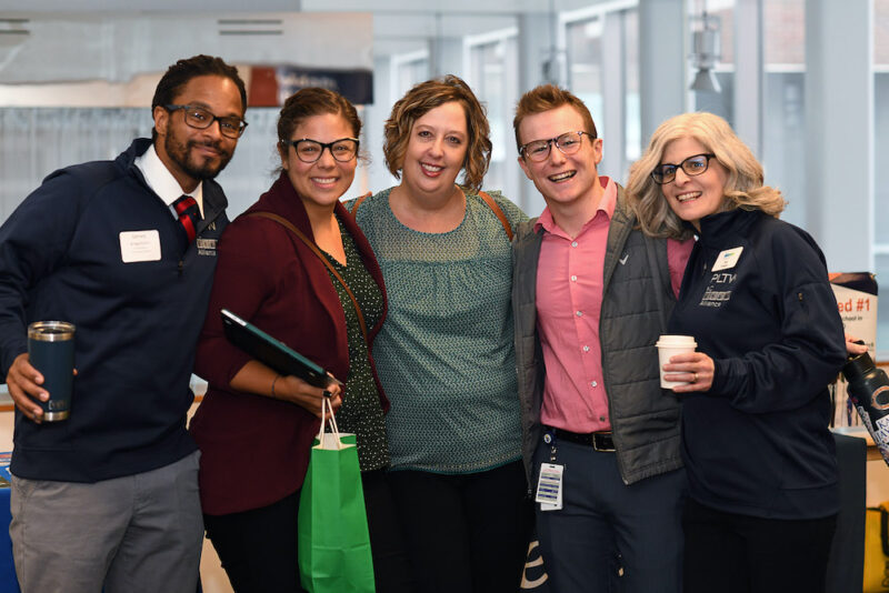 A group of five professionals smile in a posed photo at a meeting.