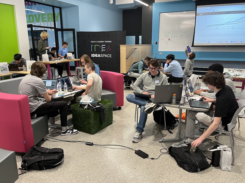Two teams of high school students work at computers in a colorful setting.
