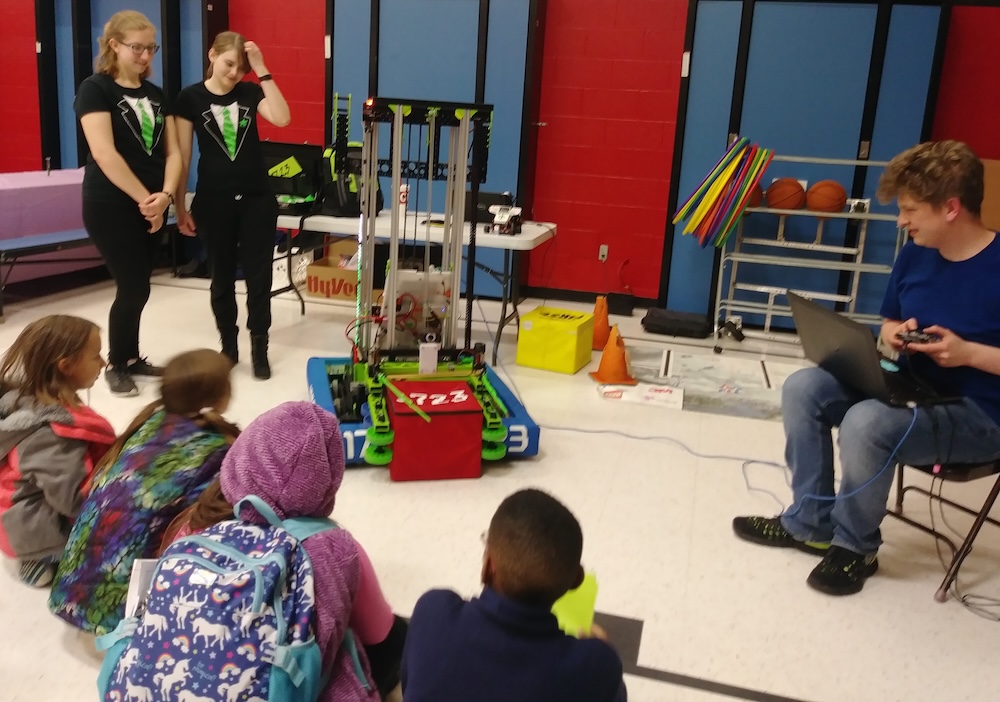 High school students show a robot to a group of elementary school students.